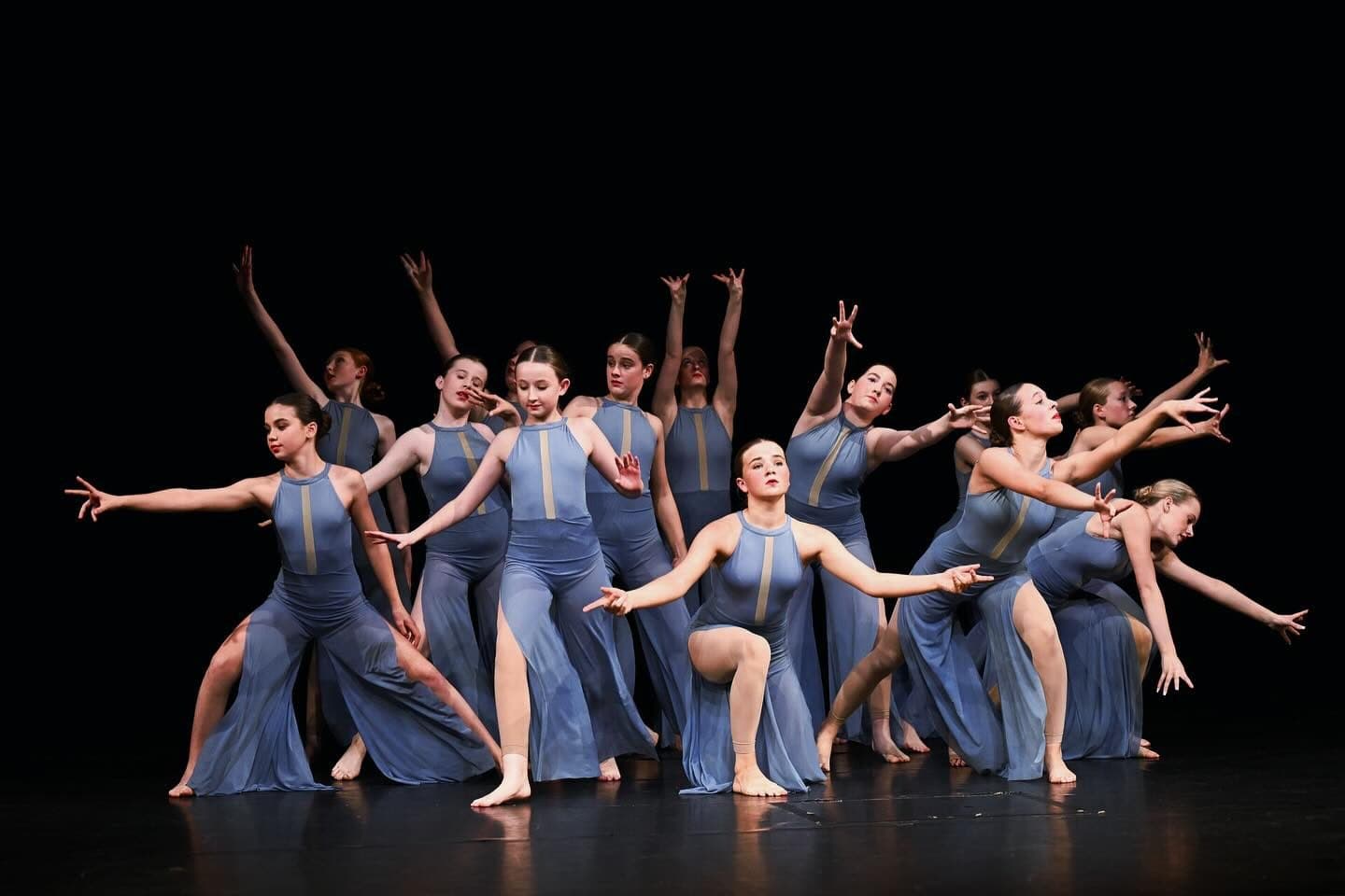 A senior ensemble holding a dynamic formation on stage, arms reaching in unison